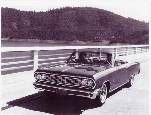 A black and white photo of a classic car on a bridge.