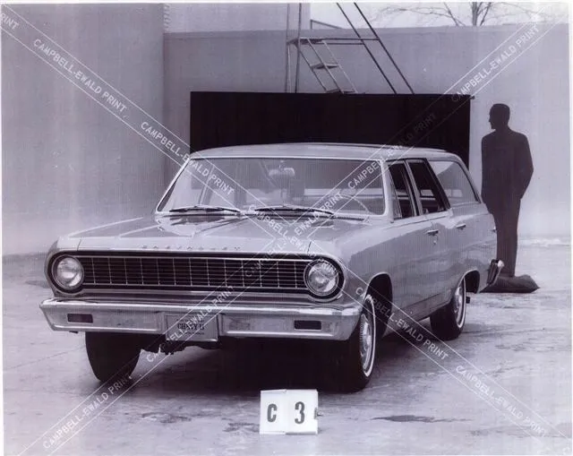A black and white photo of a station wagon with a man standing next to it.