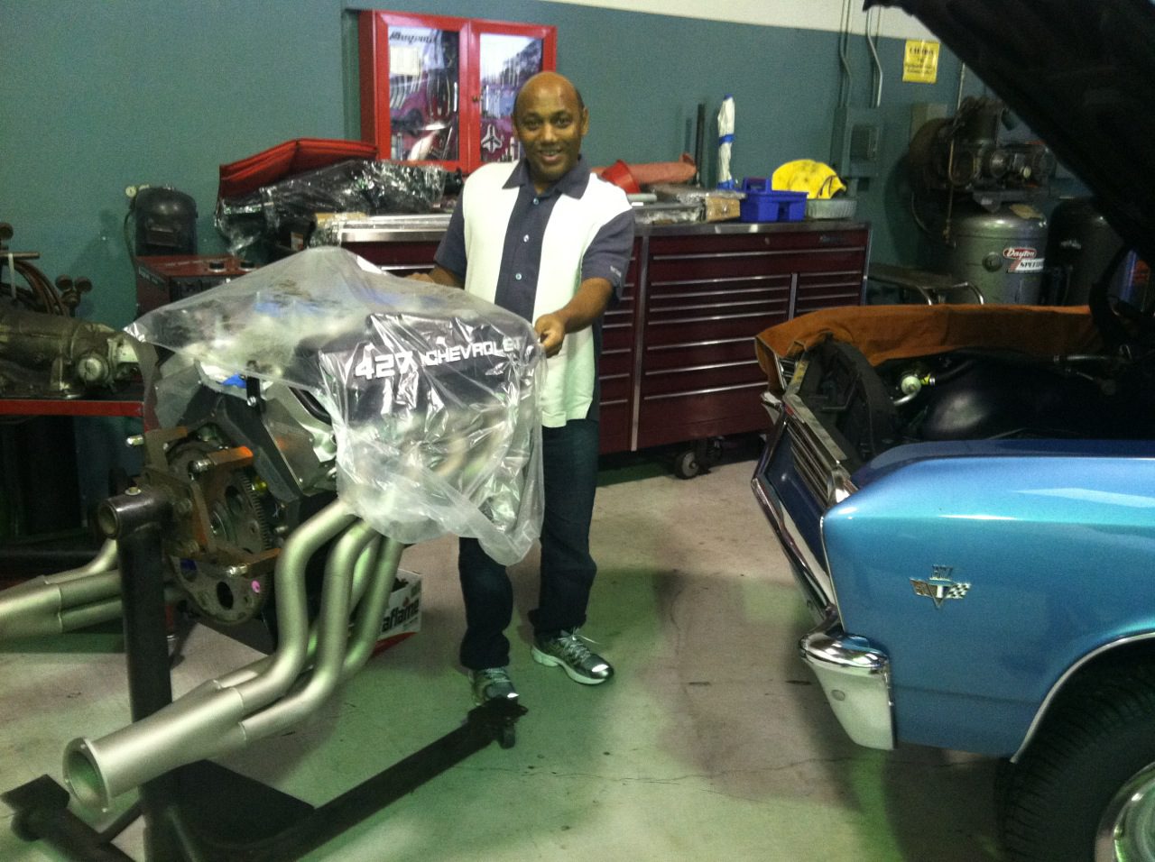 A man standing next to a blue car in a garage.