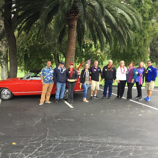 A group of people standing in front of a red car.