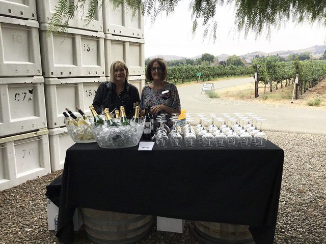 Two women standing in front of a table with wine glasses.