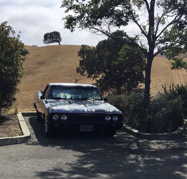 A white car parked in a parking lot next to a hill.