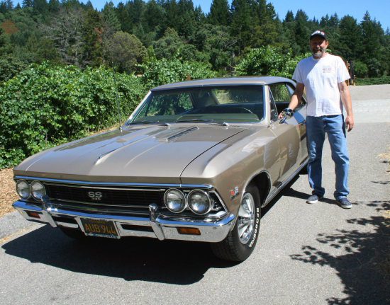 A man standing next to a tan chevrolet chevelle.