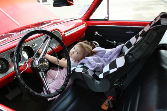 A little girl sitting in the driver's seat of a red car.