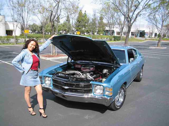 A woman standing next to a blue chevrolet chevelle.