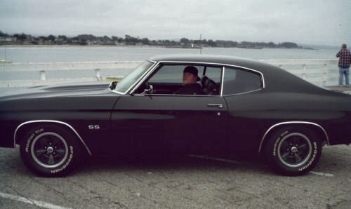 A black chevrolet chevelle parked next to the water.