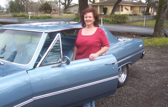 A woman standing next to a blue car.