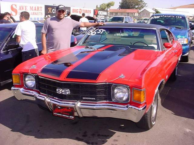 A man standing next to a red and black chevrolet chevelle.