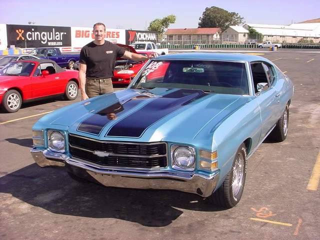 A man standing next to a blue chevrolet chevelle.