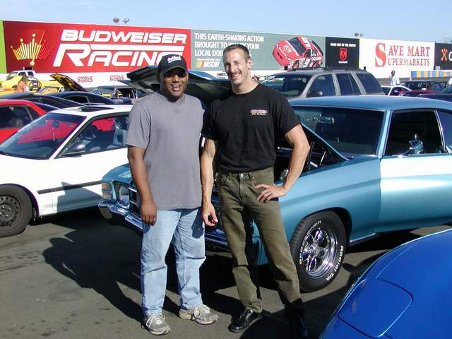 Two men standing in front of a blue car.
