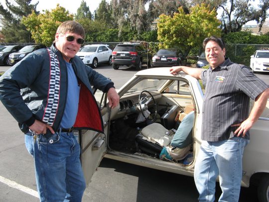 Two men standing next to a car in a parking lot.