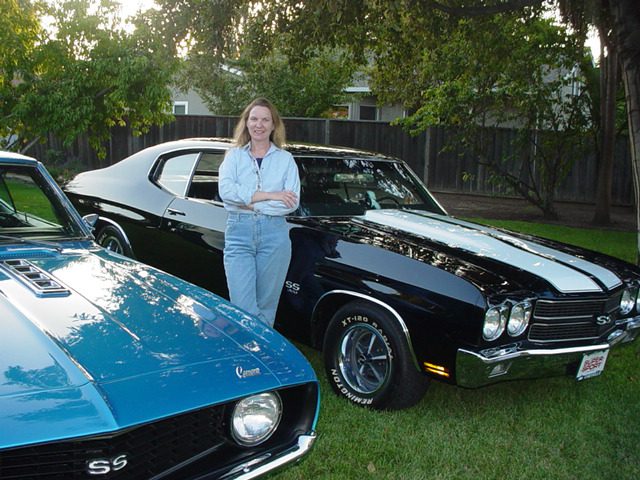 A woman standing next to a blue and black muscle car.