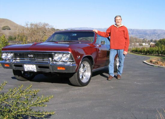 A man standing next to a red chevrolet chevelle.