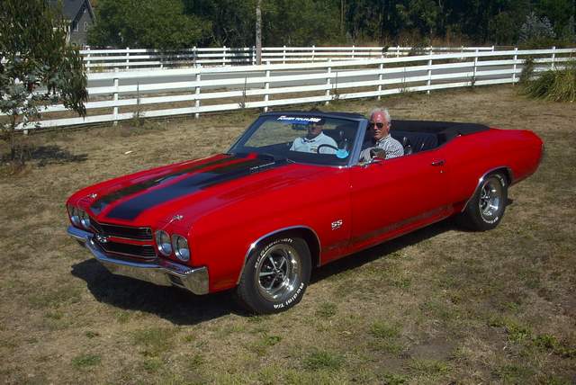A man is driving a red chevrolet chevelle in a field.