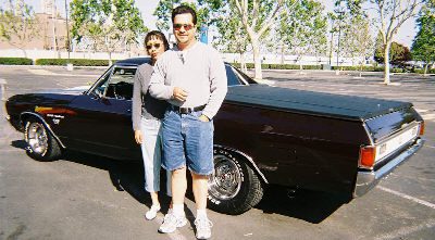A man and woman standing next to a black car.