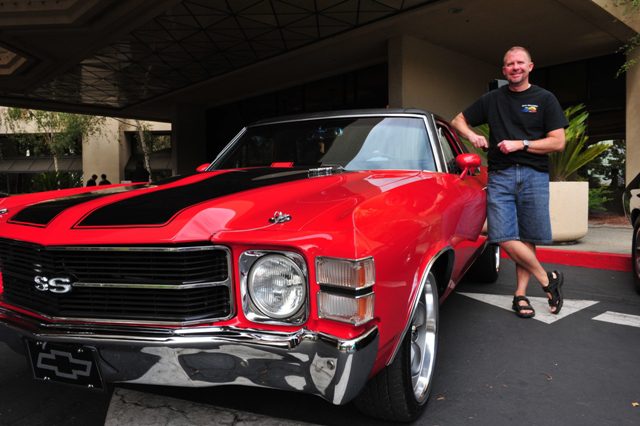 A man standing next to a red chevrolet chevelle.
