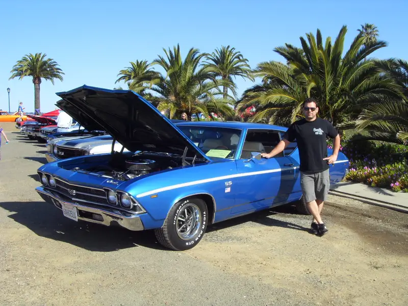 A man standing next to a blue chevrolet chevelle.